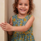Young girl wearing a blue floral dress smiling against a beige wall.
