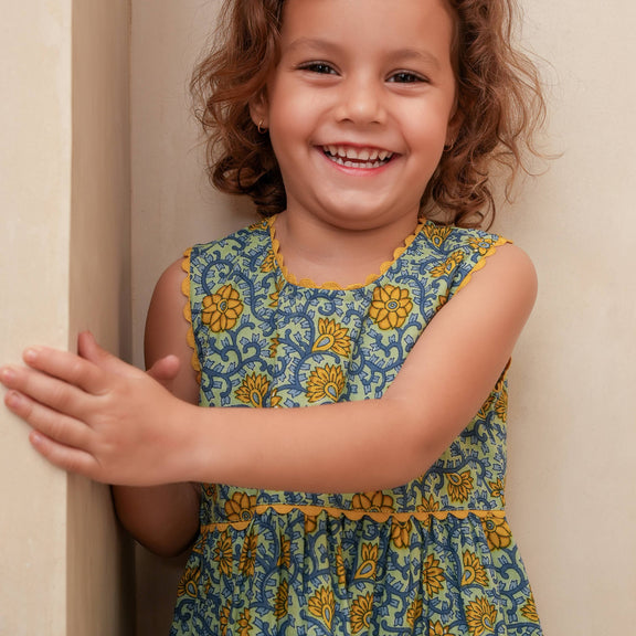 Young girl wearing a blue floral dress smiling against a beige wall.