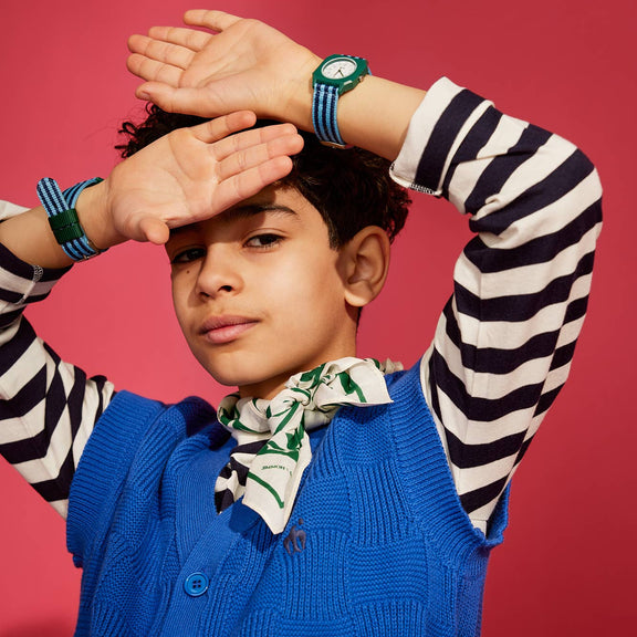 Child wearing a blue vest and striped shirt with a red background