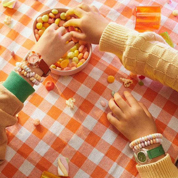 Two children playing with colorful candies on a checkered tablecloth.