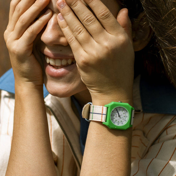 Person wearing a green watch with a striped shirt, covering their face with their hands.