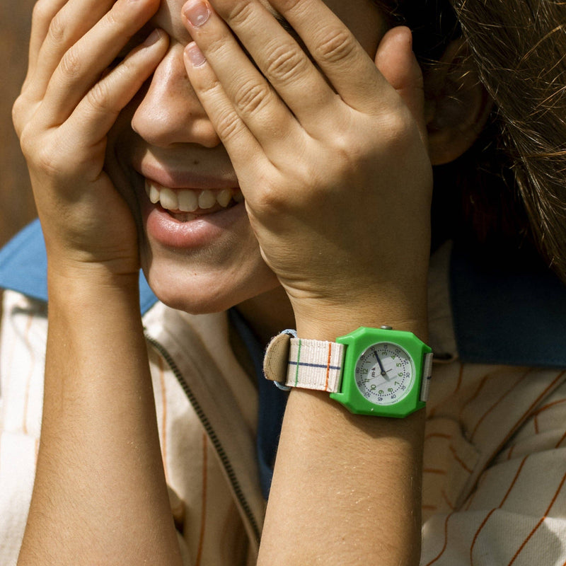 Person wearing a green watch with a striped shirt, covering their face with their hands.