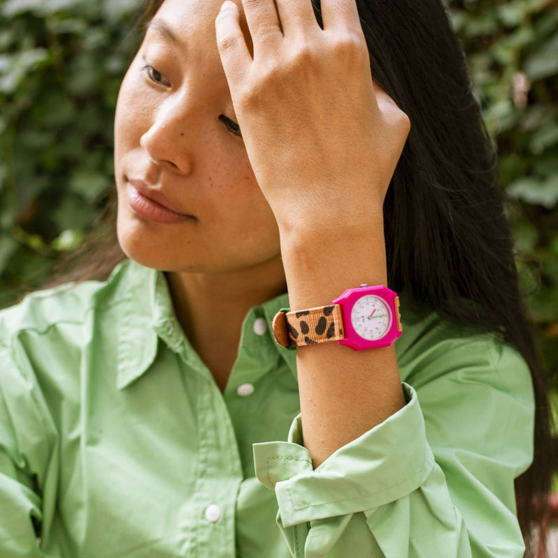Woman wearing a green shirt with a leopard print bracelet and pink watch, outdoors.