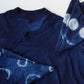 A dark indigo blue tie-dye t-shirt with matching folded fabric pieces showing white tie-dye circle patterns, laid flat on a white background.
