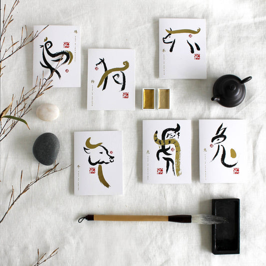 Set of cards with Chinese calligraphy on a white textured surface with a brush and stones.