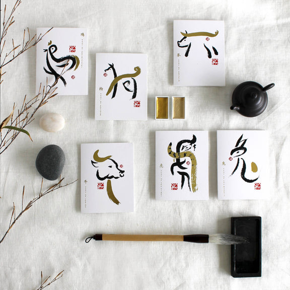 Set of cards with Chinese calligraphy on a white textured surface with a brush and stones.