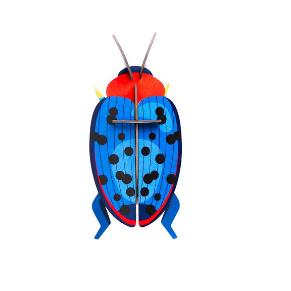 A flat-packed, colorful cardboard model of a fungus beetle, with blue body and black spots, ready to be assembled.