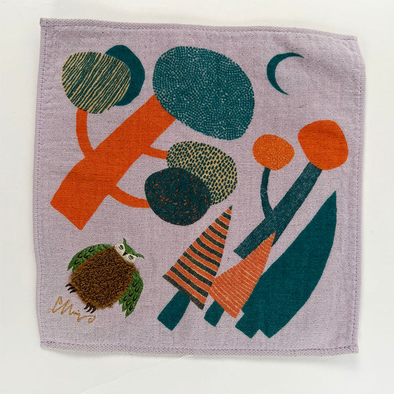 A square lavender linen cloth featuring a colorful abstract folk-art design with trees, a crescent moon, a small owl, and stylized plants, photographed flat against a white background.