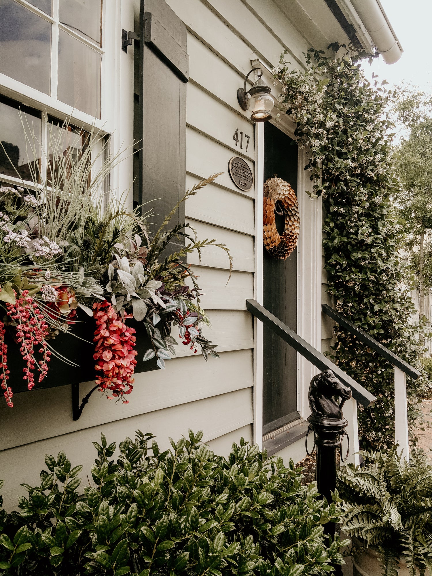 The outside of a sage green bungalo-style home with foliage around and on the windowsill