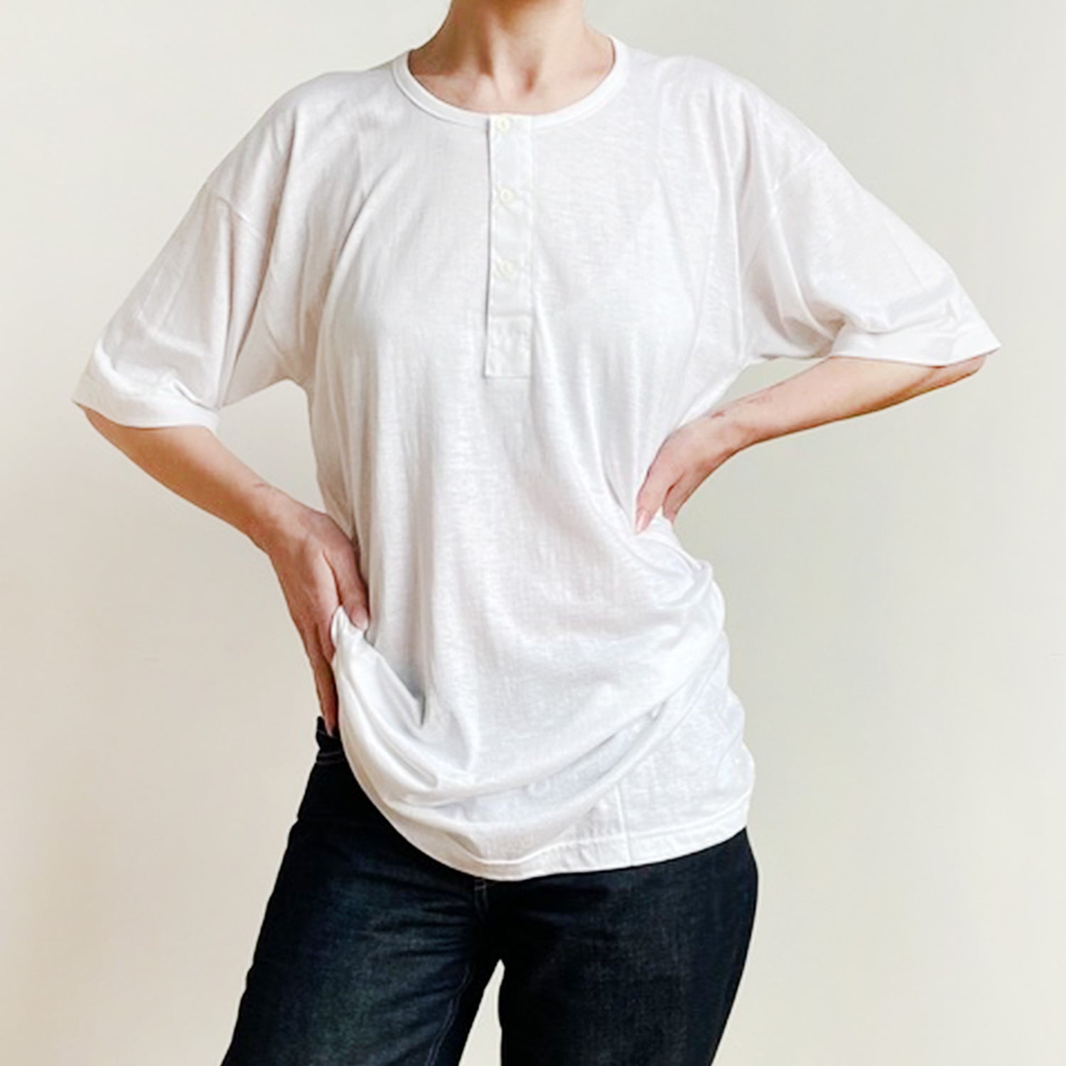 Person wearing a loose-fitting white t-shirt and dark pants on a plain background