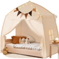 A children's play tent bed with a canopy frame, draped in cream-colored fabric, decorated with a string of warm fairy lights, a triangular pennant banner, and two plush toys on a bed. A small wooden side table with a lamp is visible next to the bed.