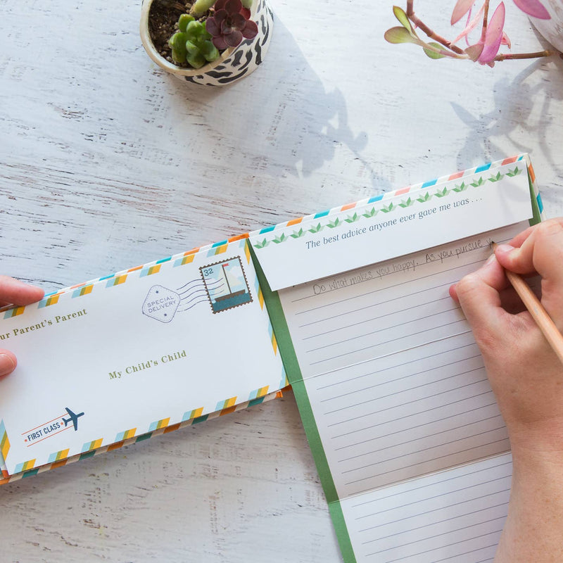 Person writing in a notebook with a decorative envelope on a light wooden surface.