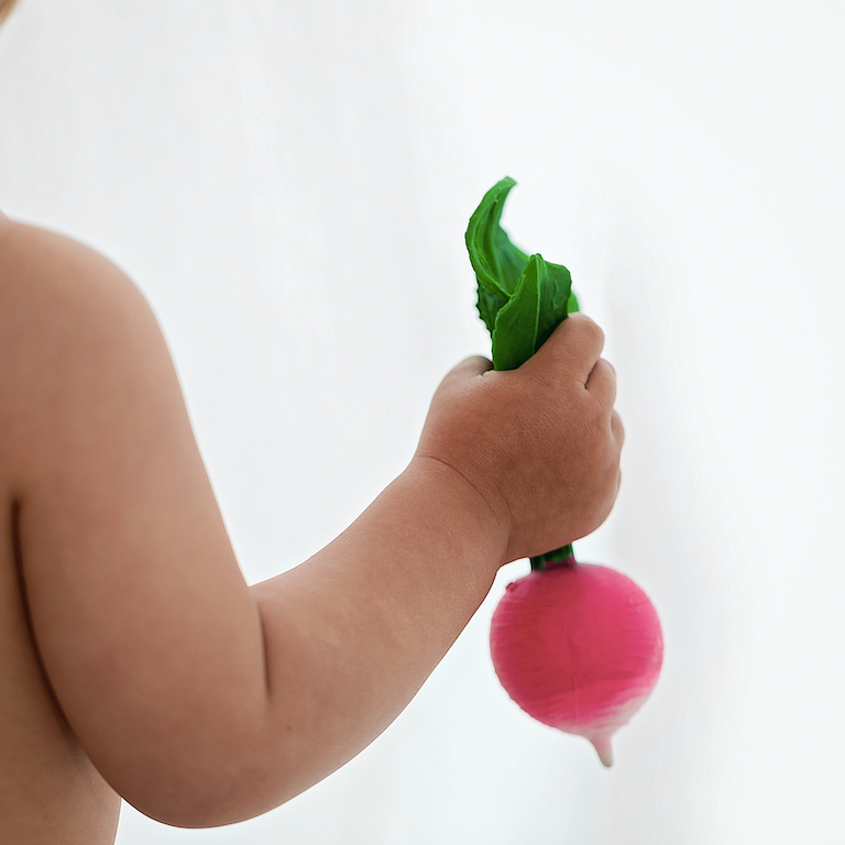 Child holding a toy radish with a pink bottom and green top against a white background