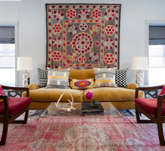 Living room with yellow sofa, colorful pillows, and a large floral tapestry.