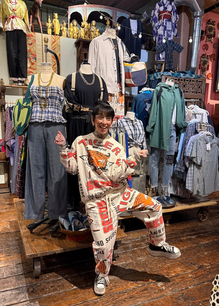 Person in a patterned outfit standing in a clothing store with various garments and accessories.